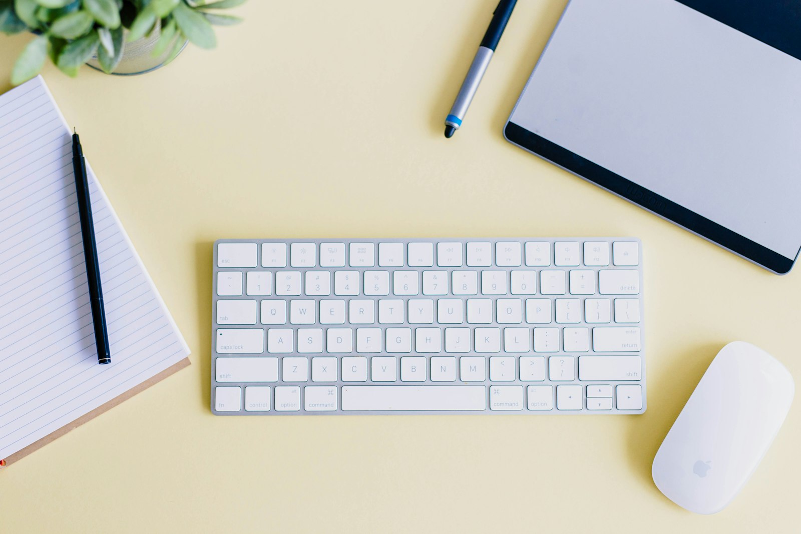 A notebook, a keyboard, and a pen arranged on a pale desk